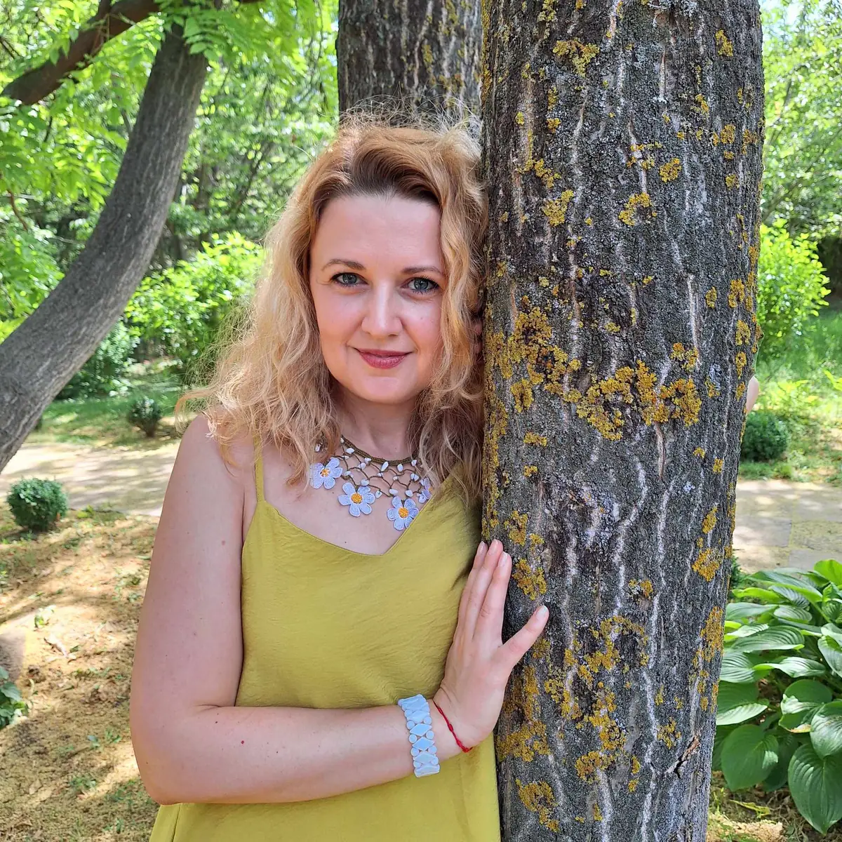 Alina Chercea resting against a tree in a sunlit garden